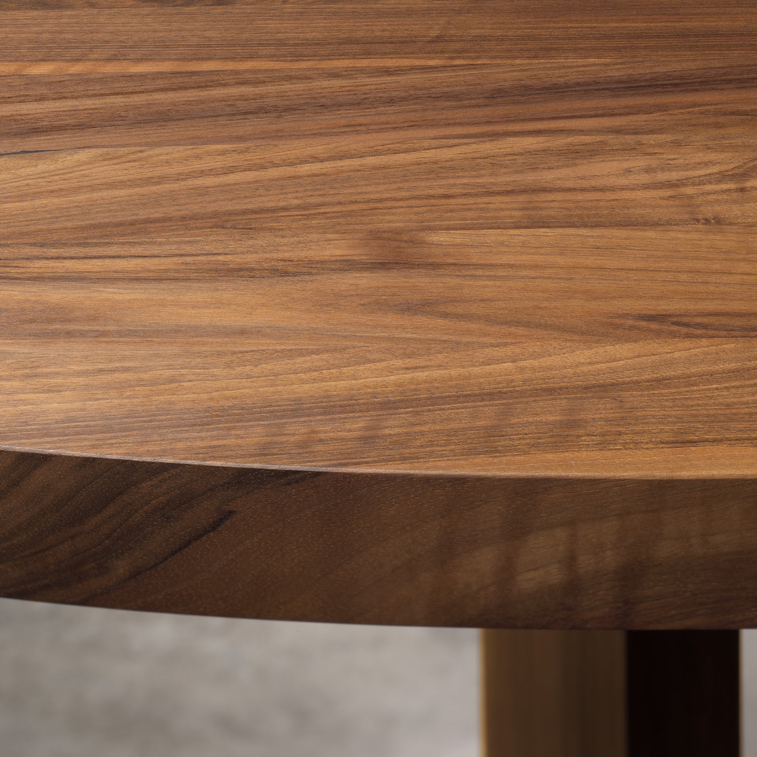 Close-up of the E15 TA24 ASHIDA Oval table, crafted from European walnut, highlighting its smooth, natural grain. The warm medium brown color with subtle variations and a glossy finish stands out against the blurred background, showcasing this masterpiece’s exquisite texture and beauty.
