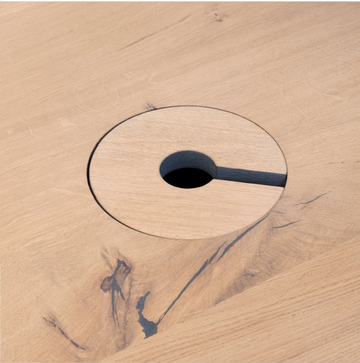 Close-up of an E15 Wire Management table surface with a round cut-out. Designed for wire management, it has a smaller circle and a slit to the edge. The wood grain and imperfections add texture, embodying the charm of customized solutions.