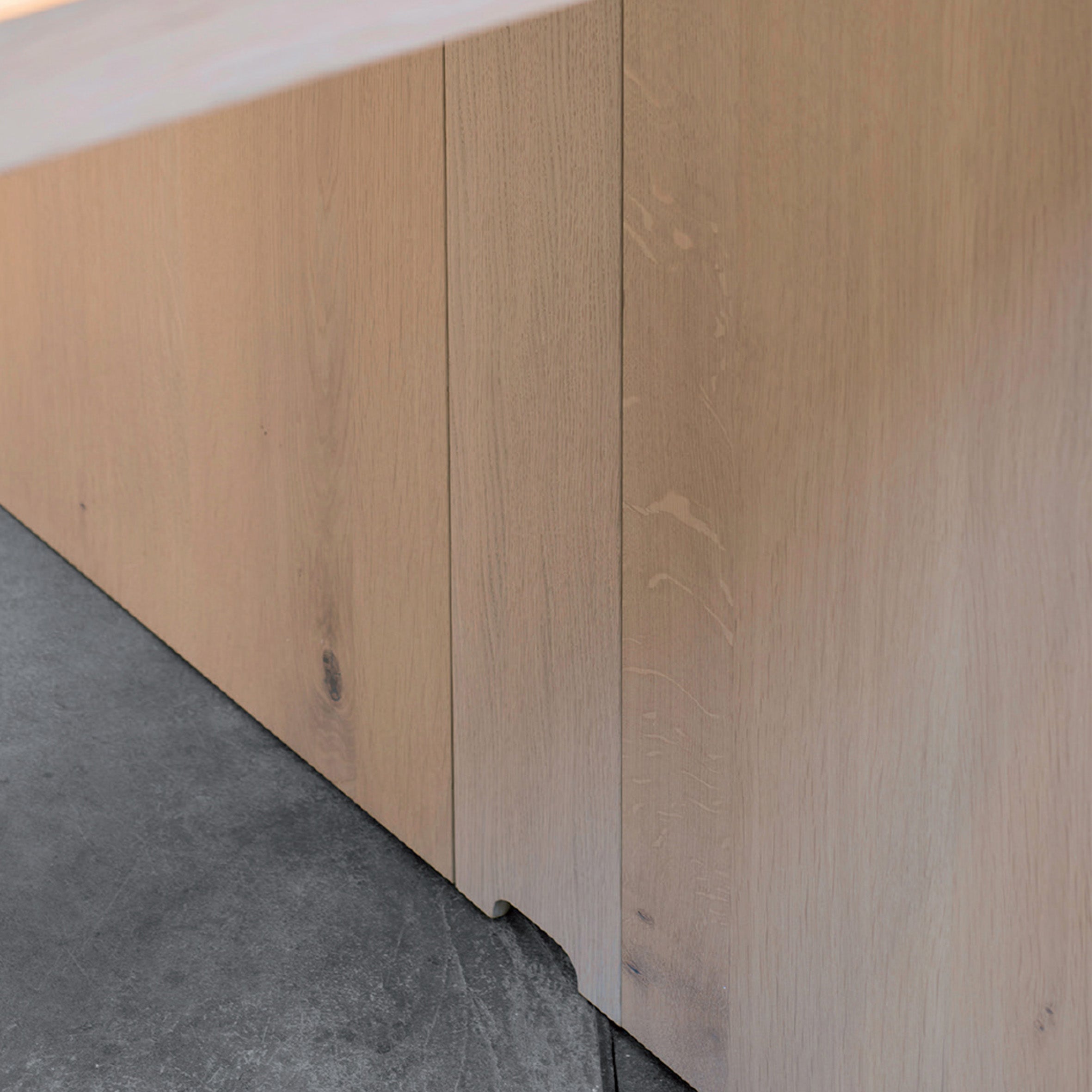 Close-up of light wood paneling extending to polished concrete, seamlessly integrating E15s Wire Management. The paneling subtly showcases wood grain and natural imperfections, echoing the minimalist and modern aesthetic of E15 tables.