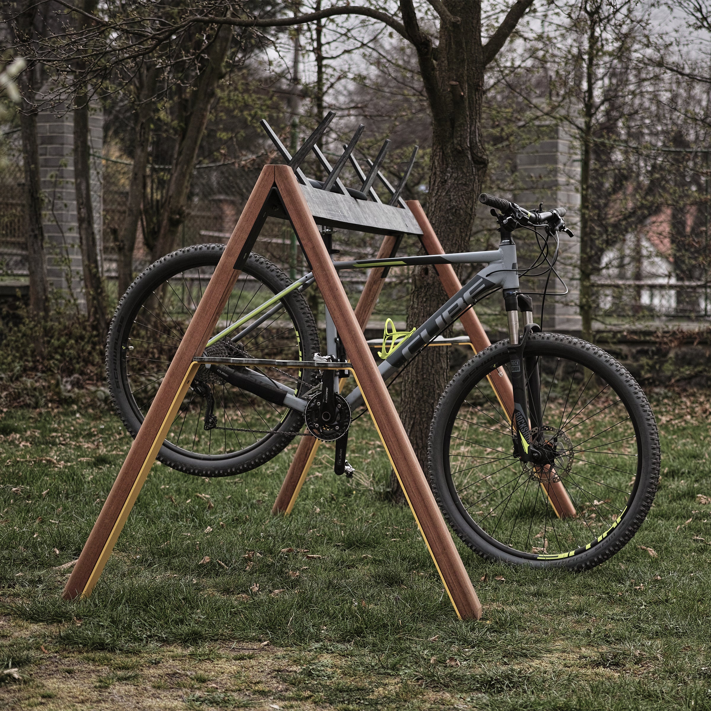 A gray and black bicycle is mounted on an Egoe Cabra Ski and Bike Rack in a grassy area with trees and a fence. The bike is elevated, suggesting it’s on display or being serviced.