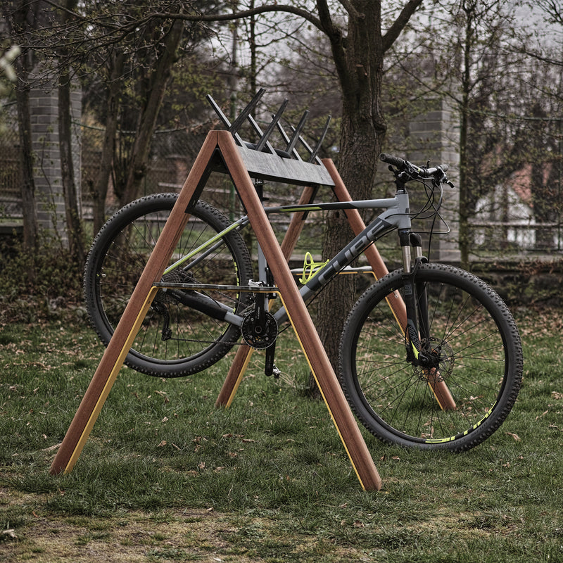 A gray and black bicycle is mounted on an Egoe Cabra Ski and Bike Rack in a grassy area with trees and a fence. The bike is elevated, suggesting it’s on display or being serviced.