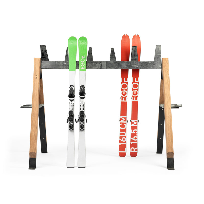 The Cabra Ski and Bike Rack by Egoe elegantly holds two pairs of skis upright, featuring green and white skis on the left, red and white marked 160 on the right with EOQE. This versatile rack displays your gear neatly and orderly.
