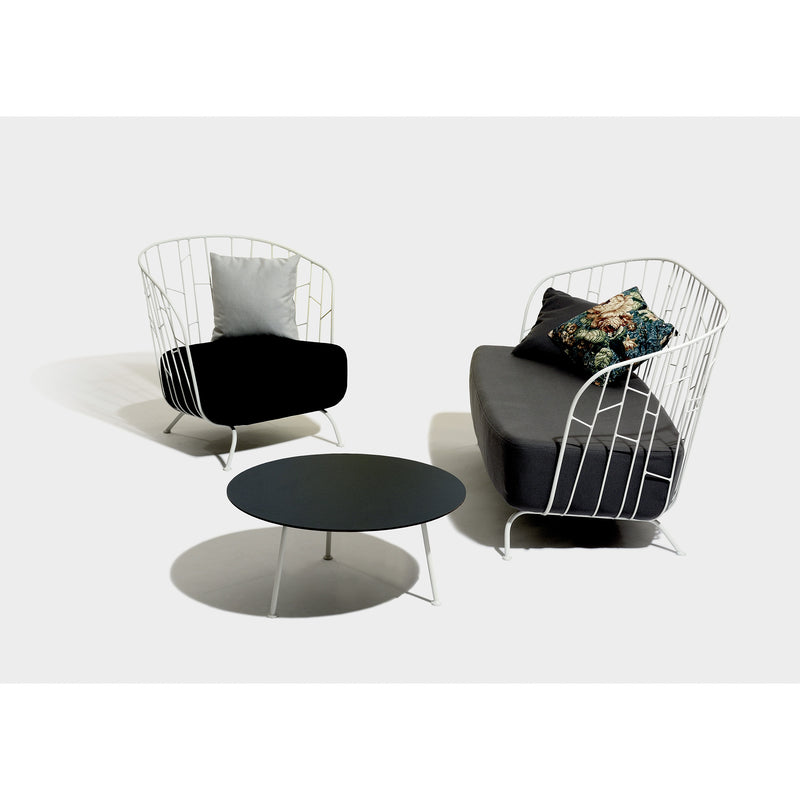 The Egoe Maj Lounge Chair is a white wireframe armchair crafted from zinc-coated steel, with a black cushion and gray pillow. Its paired with a matching loveseat featuring floral pillows and complemented by a round black coffee table, all set against a plain white background.