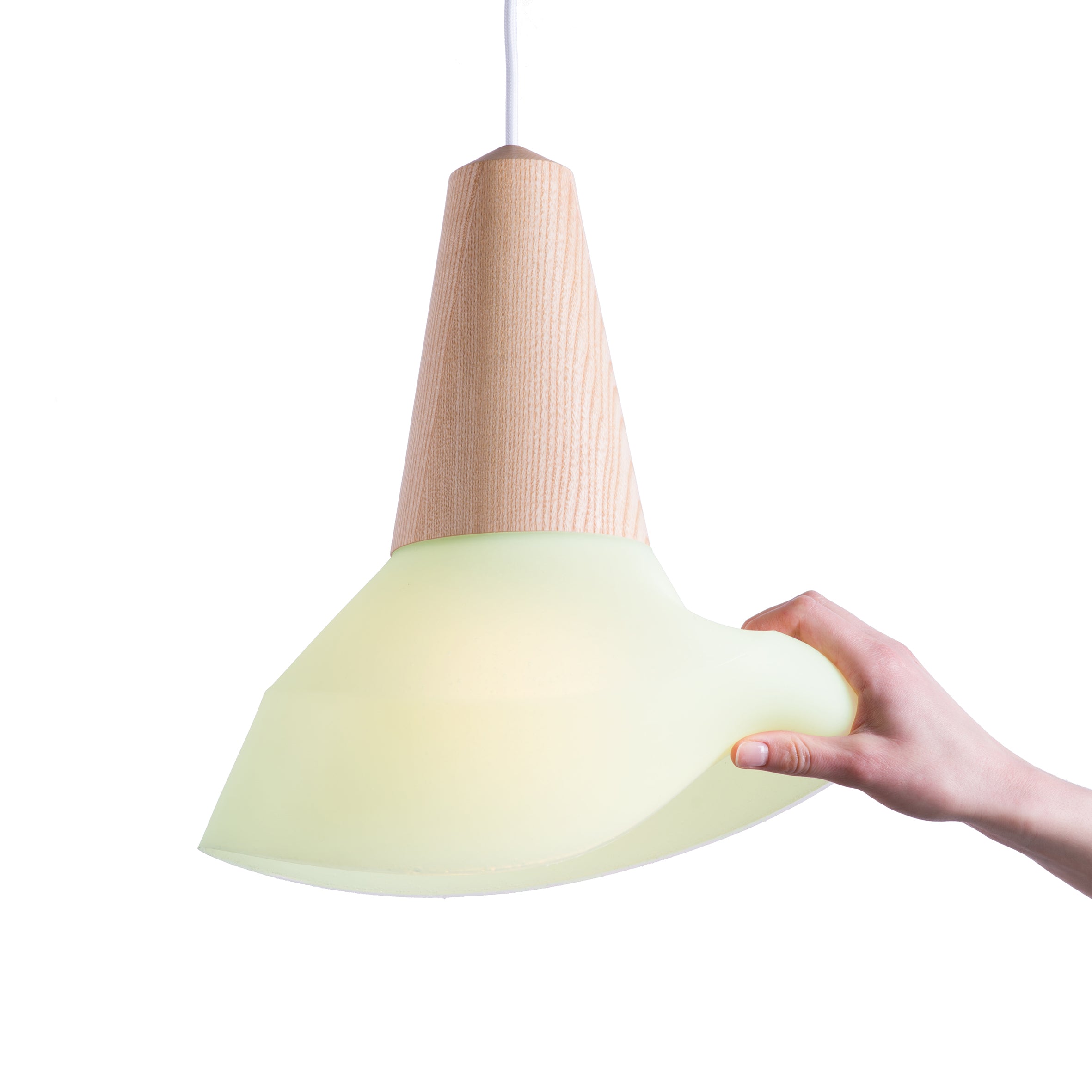 A hand holds the Schneid Eikon Bubble Mint lamp, showcasing a wooden top made from certified wood and a smooth, light green shade. The unlit pendant against a plain white background highlights its sleek design with a magnetic connecting system.