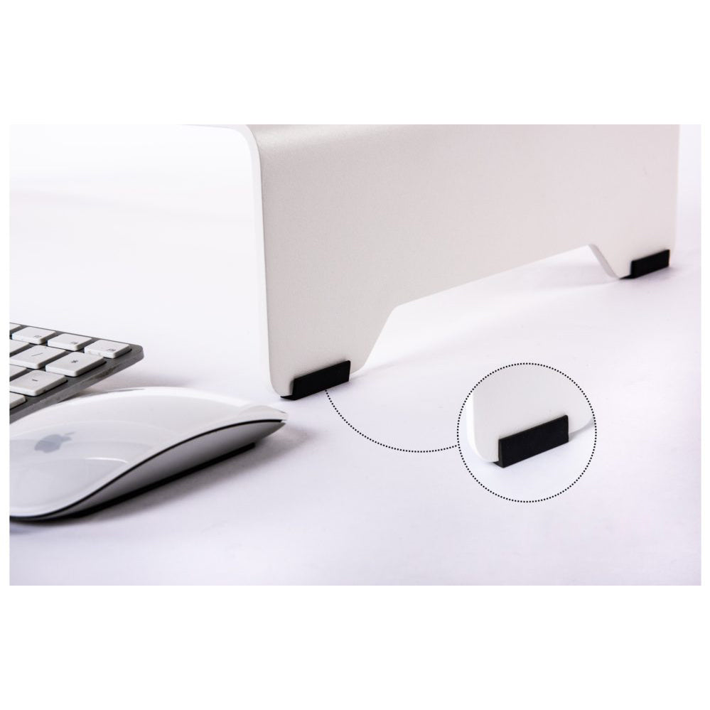 The white Echtstahl Monitor Stand, made of powder-coated steel, features a black non-slip pad for stability. A circular inset shows the pads texture. On the left, a wireless mouse and keyboard enhance ergonomic comfort on this pristine surface.