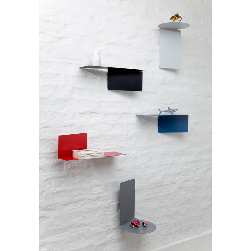 The white textured wall showcases five sophisticated Echtstahl Plateau round shelving units of various colors and shapes. Each versatile steel shelf artfully holds a distinct item: a small vase, toy, books, model airplane, and colorful balls for a modern aesthetic.