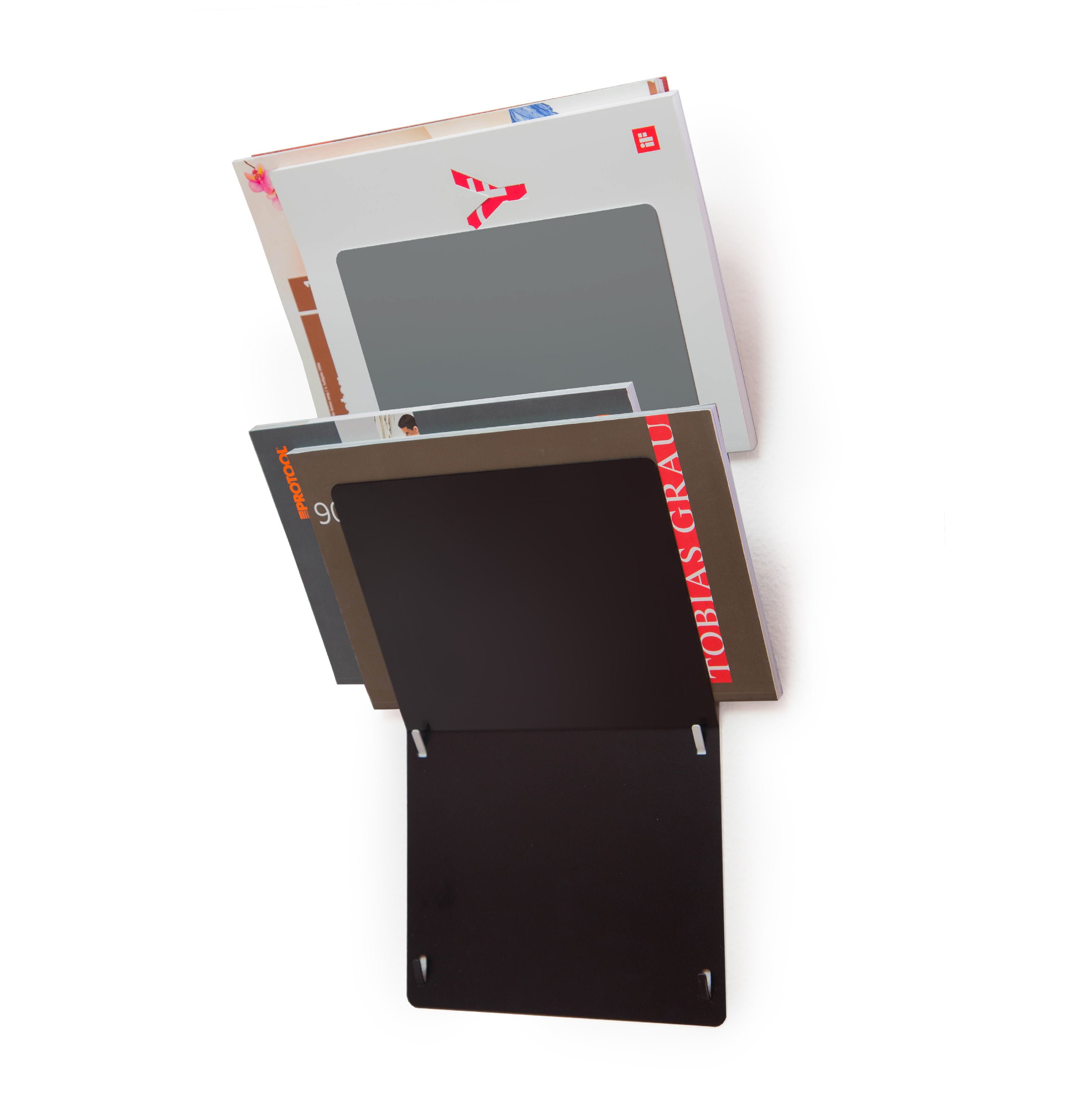 The Trik by Echtstahl is a wall-mounted, minimalist magazine rack in sleek black stainless steel with two compartments for books and magazines. This elegant storage solution displays covers prominently, featuring the top magazine with a large red logo.