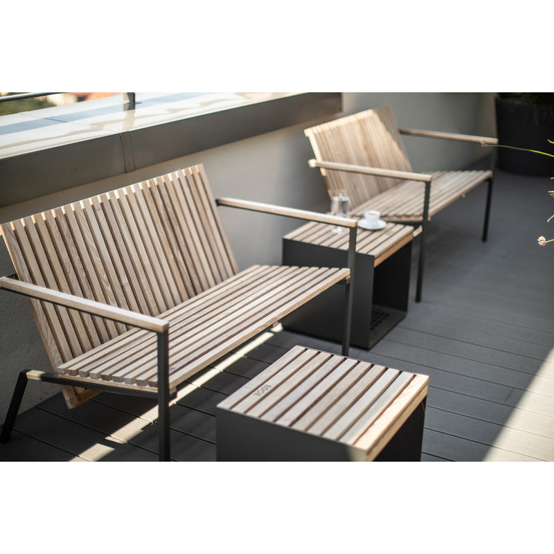 A patio awash with sunlight features Egoes Axis Lounge Armchair series with two slatted wooden benches. Between them is a small square table made from zinc-plated steel, holding a glass and cup with saucer, all set on sleek grey deck flooring.