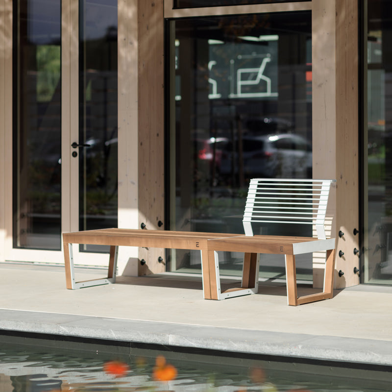 The Barka Public Chair by Egoé, featuring Jatoba wood and zinc-coated steel, adorns the concrete patio. Facing a pool with orange fish, it complements the scene where glass doors reflect blurred images of parked cars.