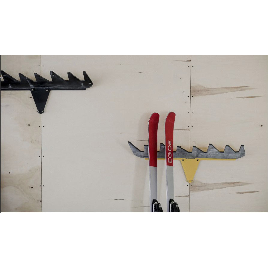 The Jelen Ski Rack by Egoe elegantly displays skis on the wall, featuring distinctive black, yellow, and gray accents. The red and white patterned skis contrast beautifully against light wooden panels, offering a striking storage solution for ski enthusiasts.