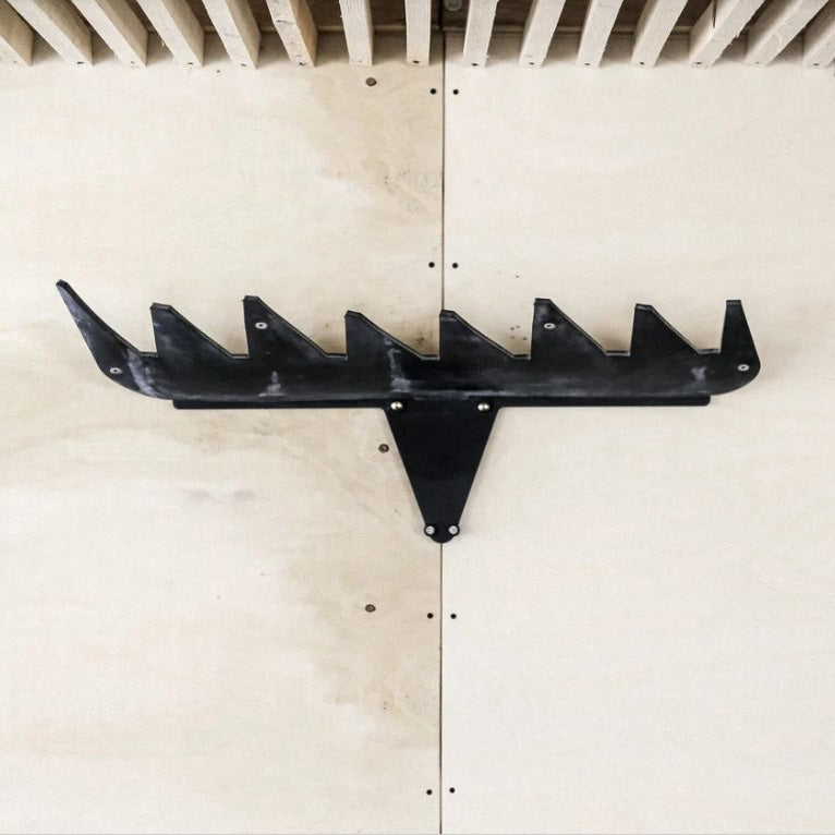 The Jelen Ski Rack by Egoe is a black, geometric wall sculpture resembling a stylized animal head with upward-facing triangles that cleverly conceals a ski rack. Mounted on a light wooden wall with a slatted ceiling above, it seamlessly blends art with practical ski storage.