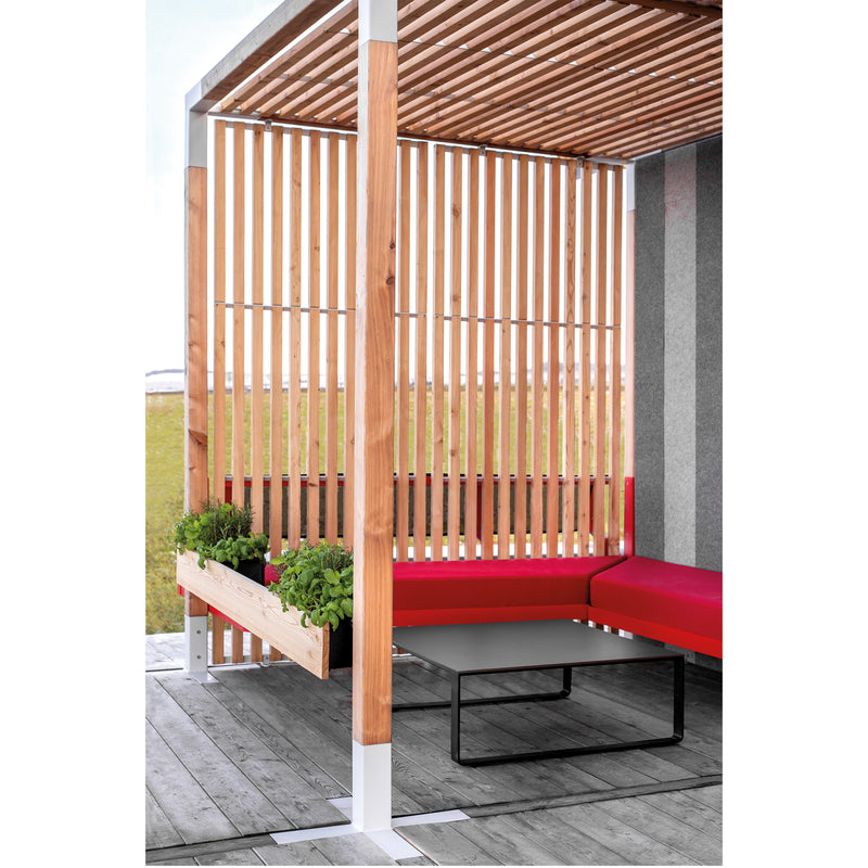Egoés Leva Office and Classroom system includes red cushioned benches encircling a square gray table, with wooden slats forming a partial roof and wall for a modern outdoor seating area. A planter box adds greenery to this ideal outdoor office setting on the wooden deck.