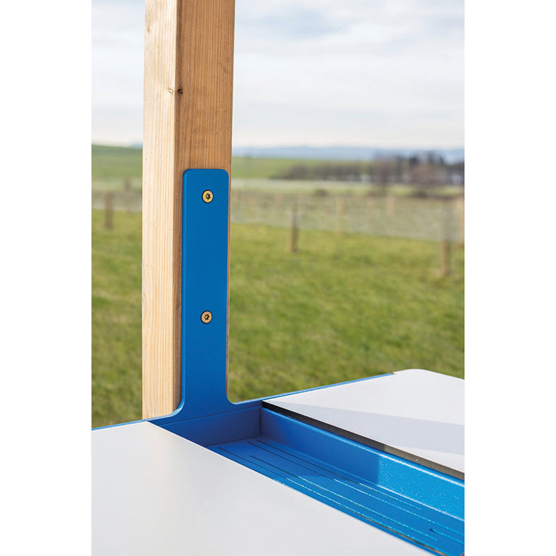 A close-up of a blue and white Leva Office desk by Egoé, attached to a wooden post in a grassy field with a blurred fence and horizon. The overcast sky adds to the serene countryside vibe, ideal for an outdoor office setup.