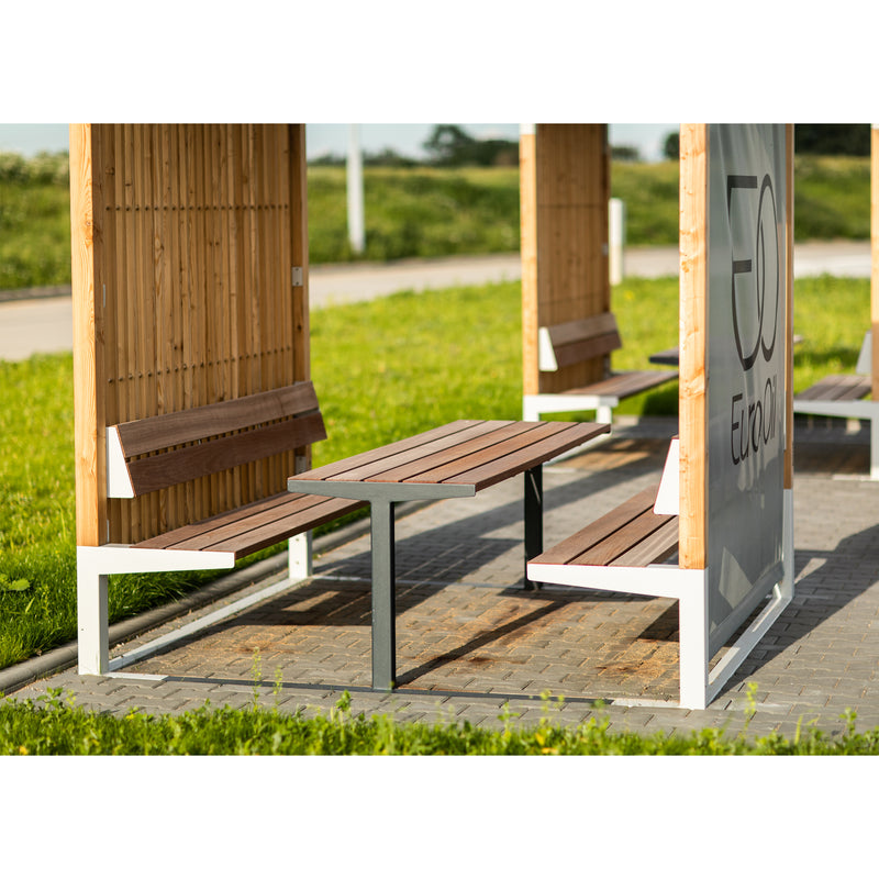 The Leva Public by Egoe creates a modern outdoor seating area with wooden benches and tables under partial shade. This sunlit space, enriched with green grass and a paved walkway, seamlessly becomes an inviting open-air office.