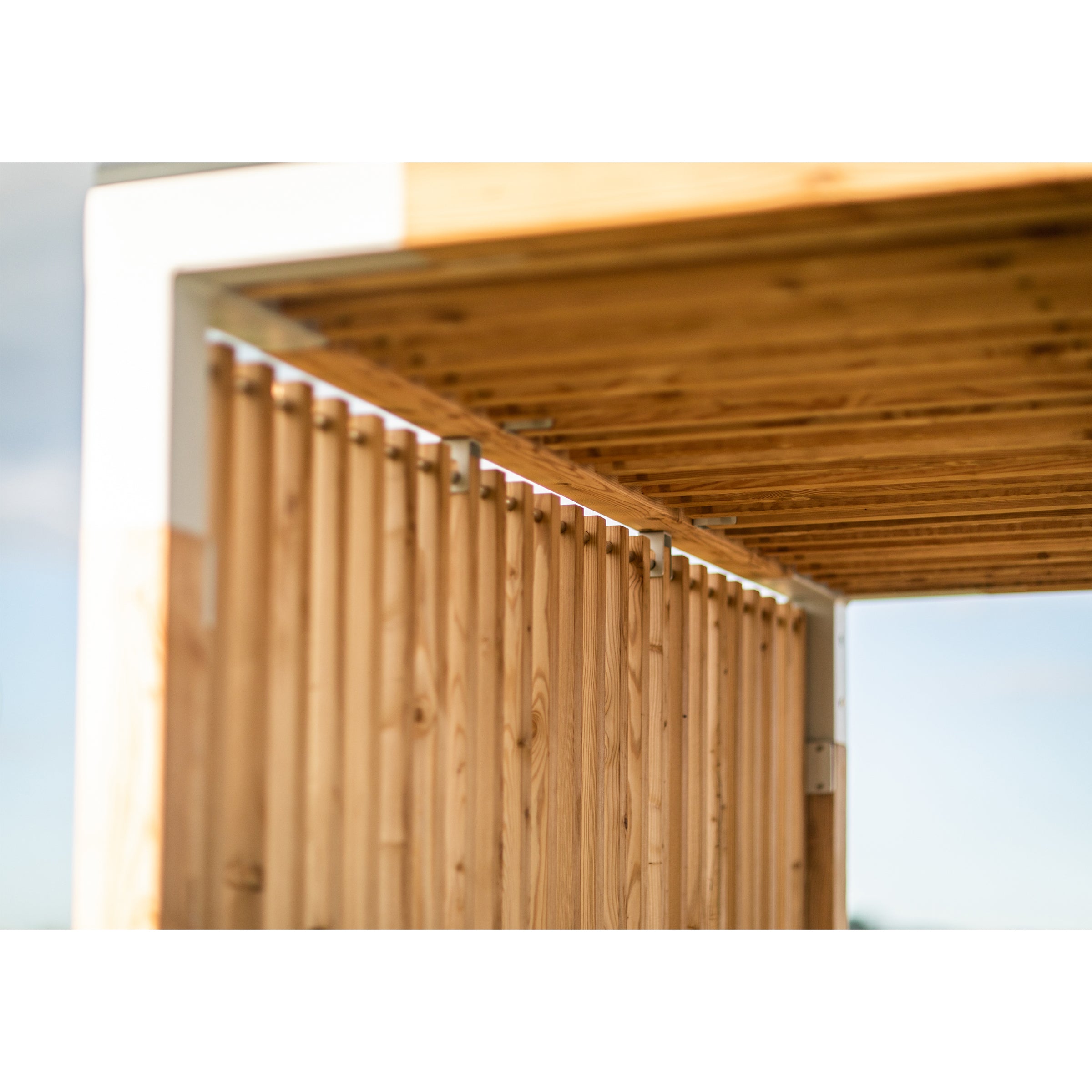 Close-up of the Leva Public wooden pergola by Egoé. The image highlights intersecting beams and slats, showcasing the natural wood grain. A softly blurred background accentuates the architectural details and warm tones, making it an ideal outdoor office setting.