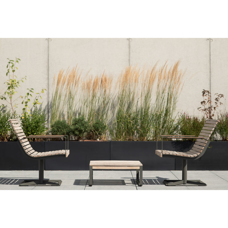 Two Preva Armchairs by Egoe flank a small table on the patio. They are backed by tall ornamental grasses and greenery in planters against a light concrete wall, creating a sophisticated and minimalistic escape.