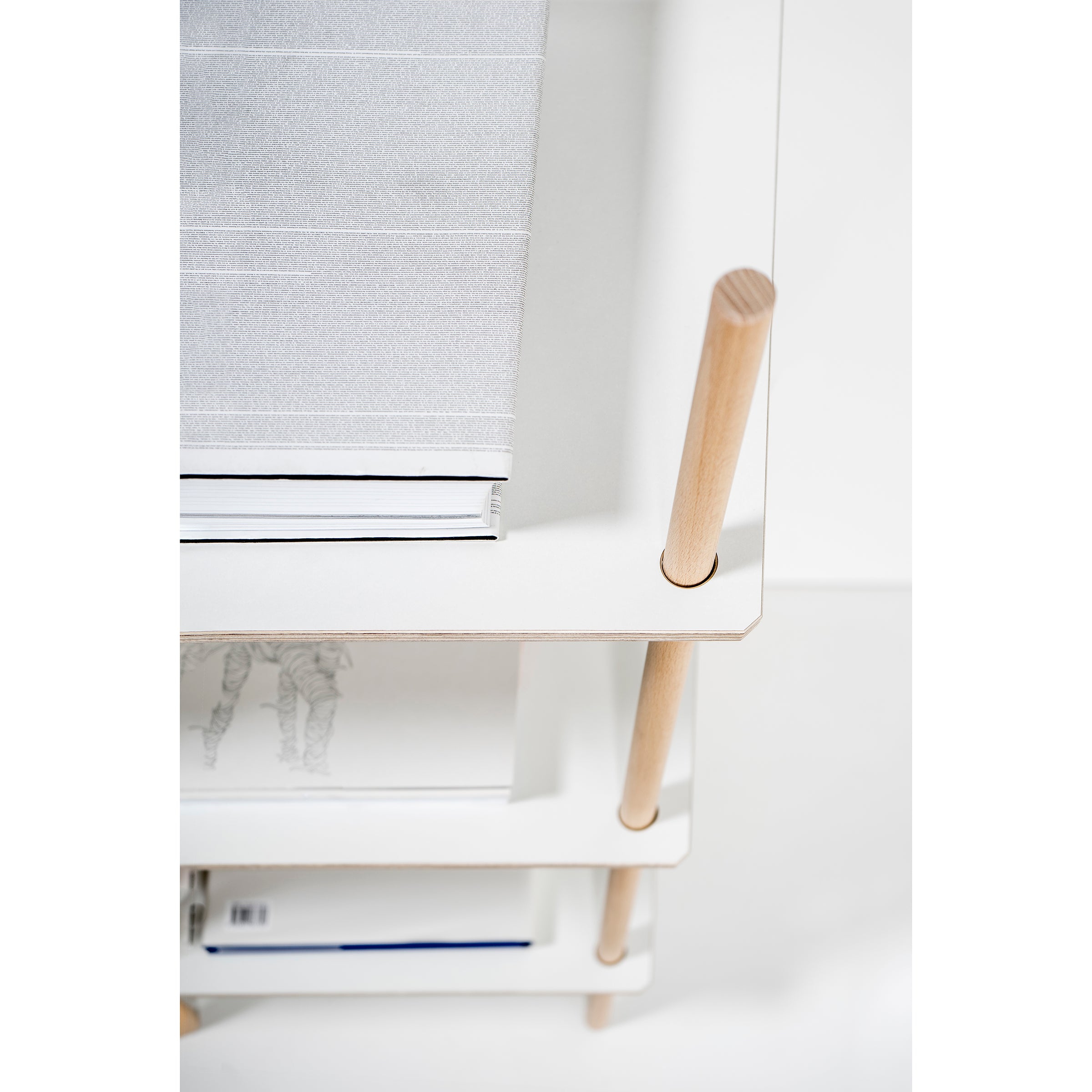 Top view of the Es Sideboard by Moormann, featuring minimalist birch plywood boards with precise craftsmanship. A sleek white surface with wooden legs holds a gray book, while lower shelves accommodate various books, magazines, and assorted items.