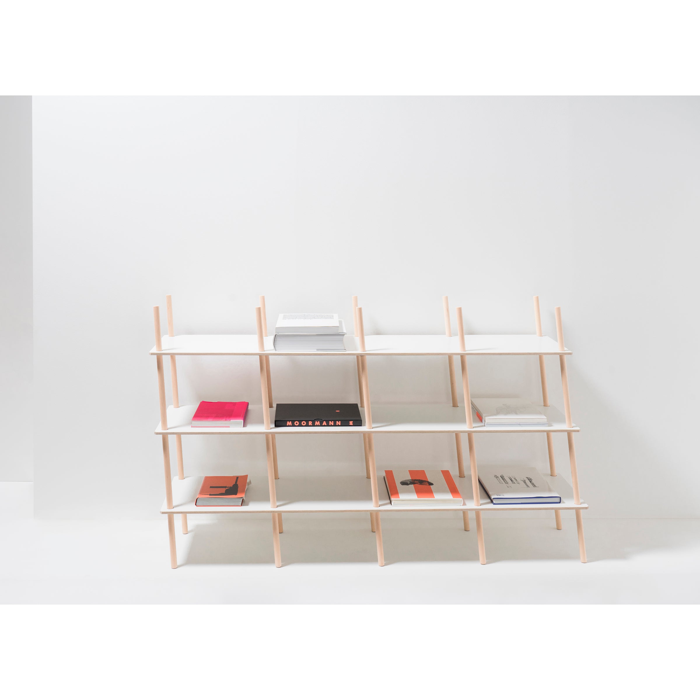 The Moormann Es Sideboard is a minimalist piece crafted from birch plywood, characterized by a precise grid design for holding books and small objects. Its light wood and white surfaces elegantly complement a plain white wall in a well-lit room.