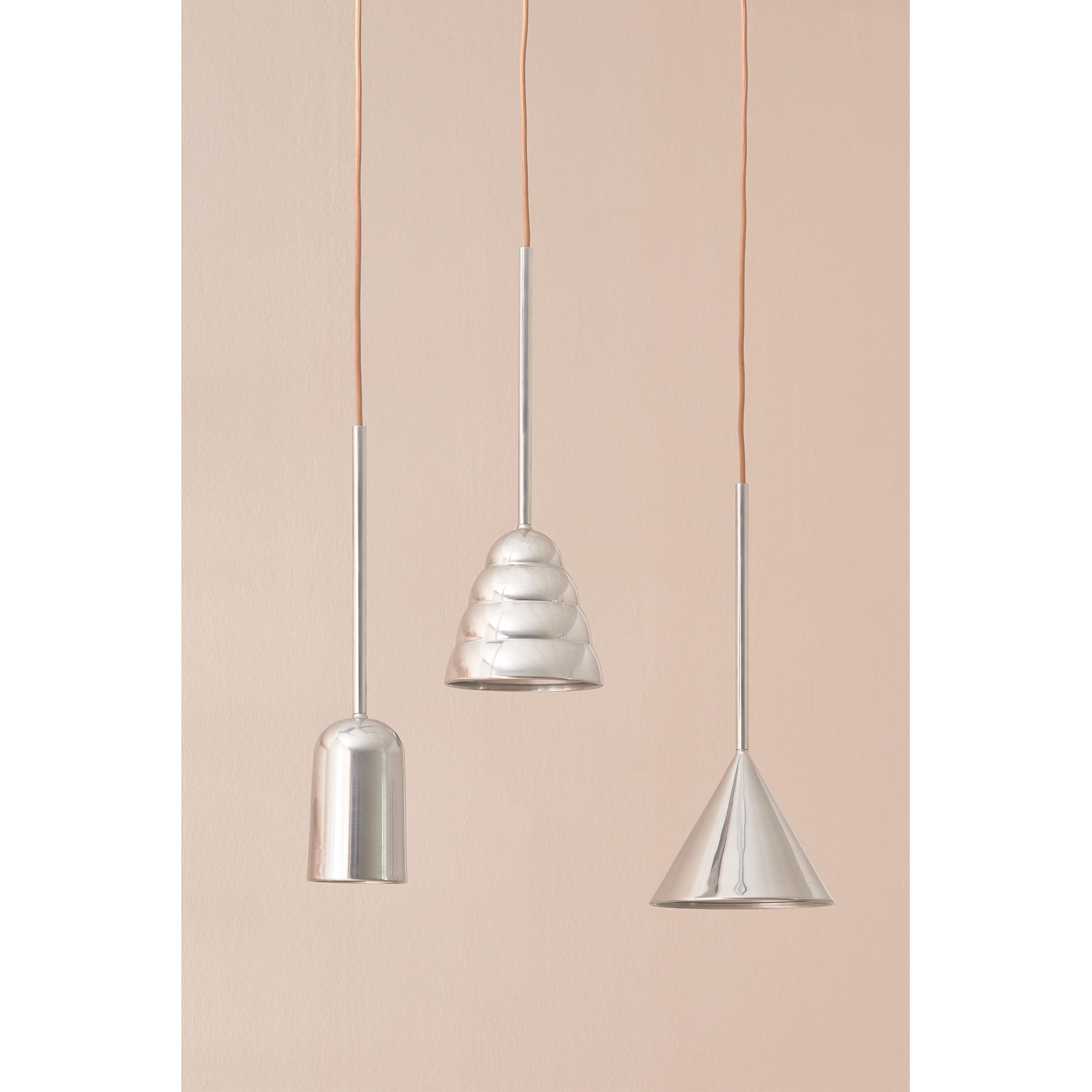 Three modern Schneid pendant lights with sculptural silhouettes hang against a beige background. Each luminaire has a unique metallic shape, including the Figura Cone Chrome. Theyre suspended by thin cords: one is smooth and elongated, another resembles a spiral shell, and the last is conical.