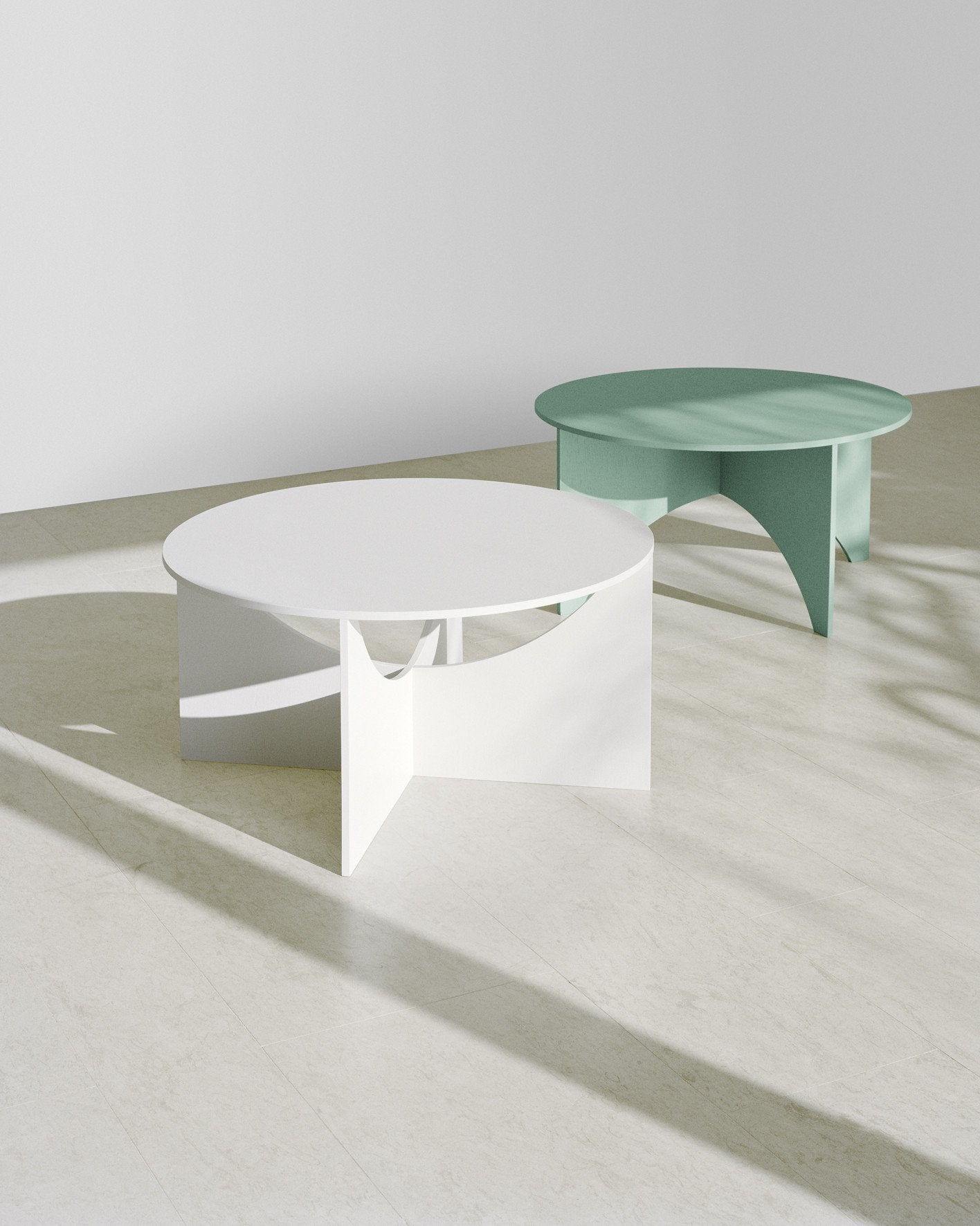 Two FK05 CHARLOTTE tables by E15 enhance a minimalist room; the foreground table is white with a geometric base, and the background one is green with a similar design. Both cast soft shadows on the light-colored floor, highlighting Ferdinand Kramers famed aesthetic.