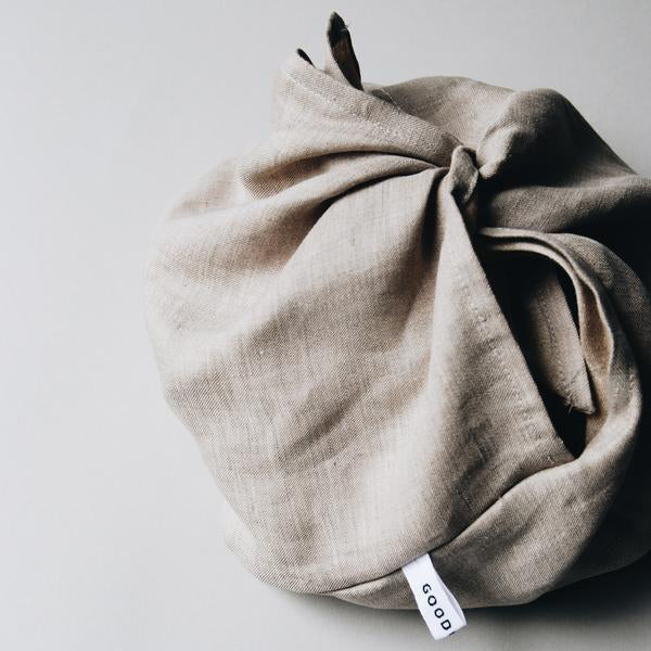 A Bento by GoodGoods, a beige cloth bundle tied at the top with a Good label, sits elegantly on a light gray surface.