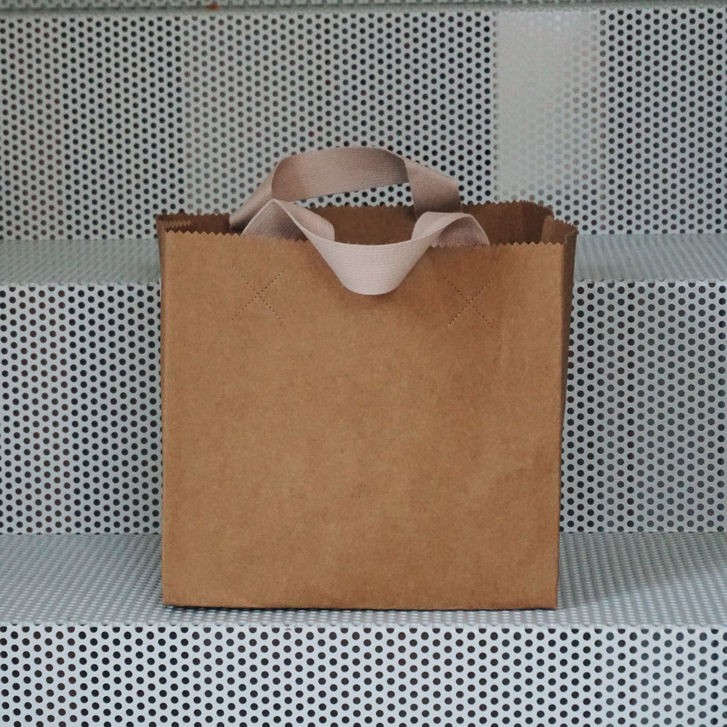 A GoodGoods Box Bag, resembling a foldable tote bag, sits on perforated metal steps.