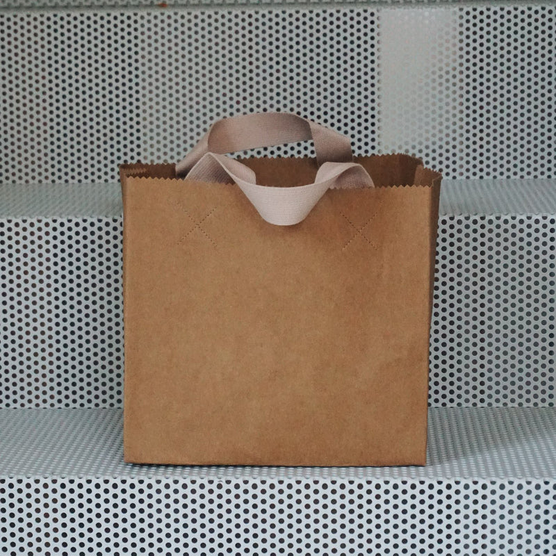 A GoodGoods Box Bag, resembling a foldable tote bag, sits on perforated metal steps.