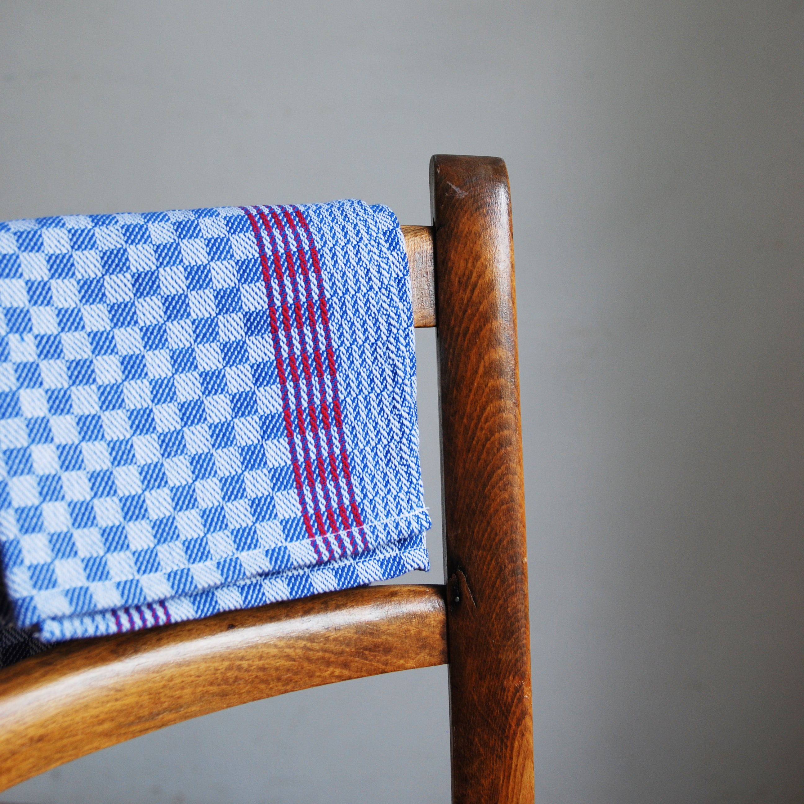 A blue and white checkered cotton cloth with red stripes, draped over a wooden chair against a light gray background, captures the essence of GoodGoods sturdy Dry dish towel.