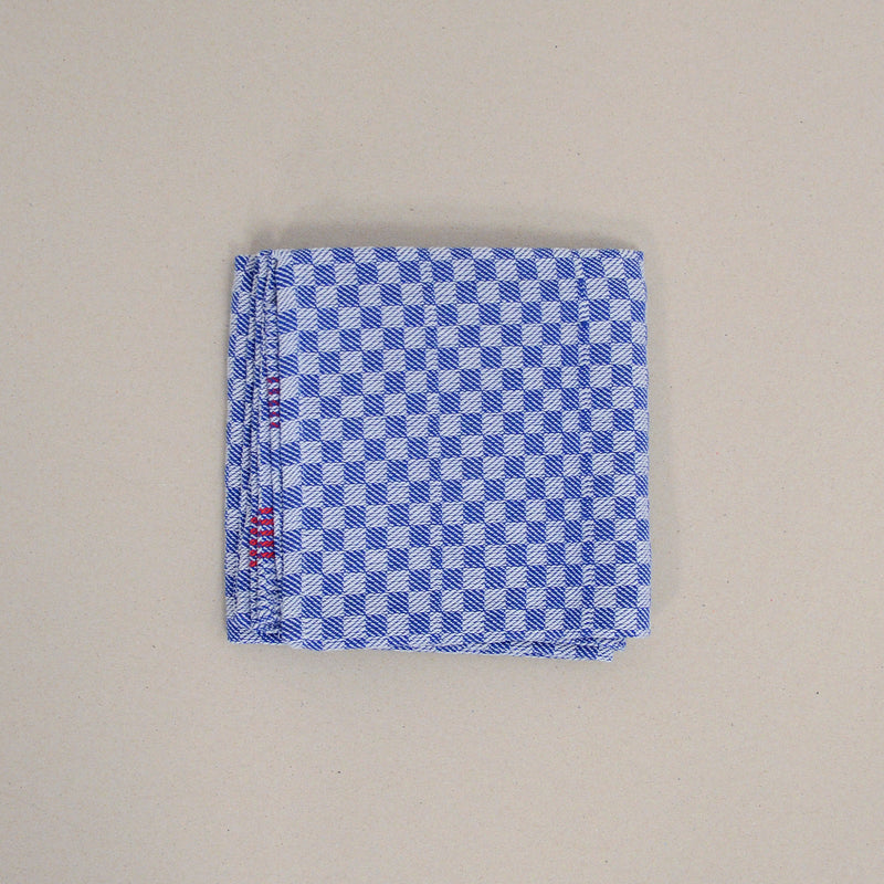 The product Dry by GoodGoods features a neatly folded cotton handkerchief in blue and white checkered pattern with a red detail at one corner, displayed on a plain beige background.