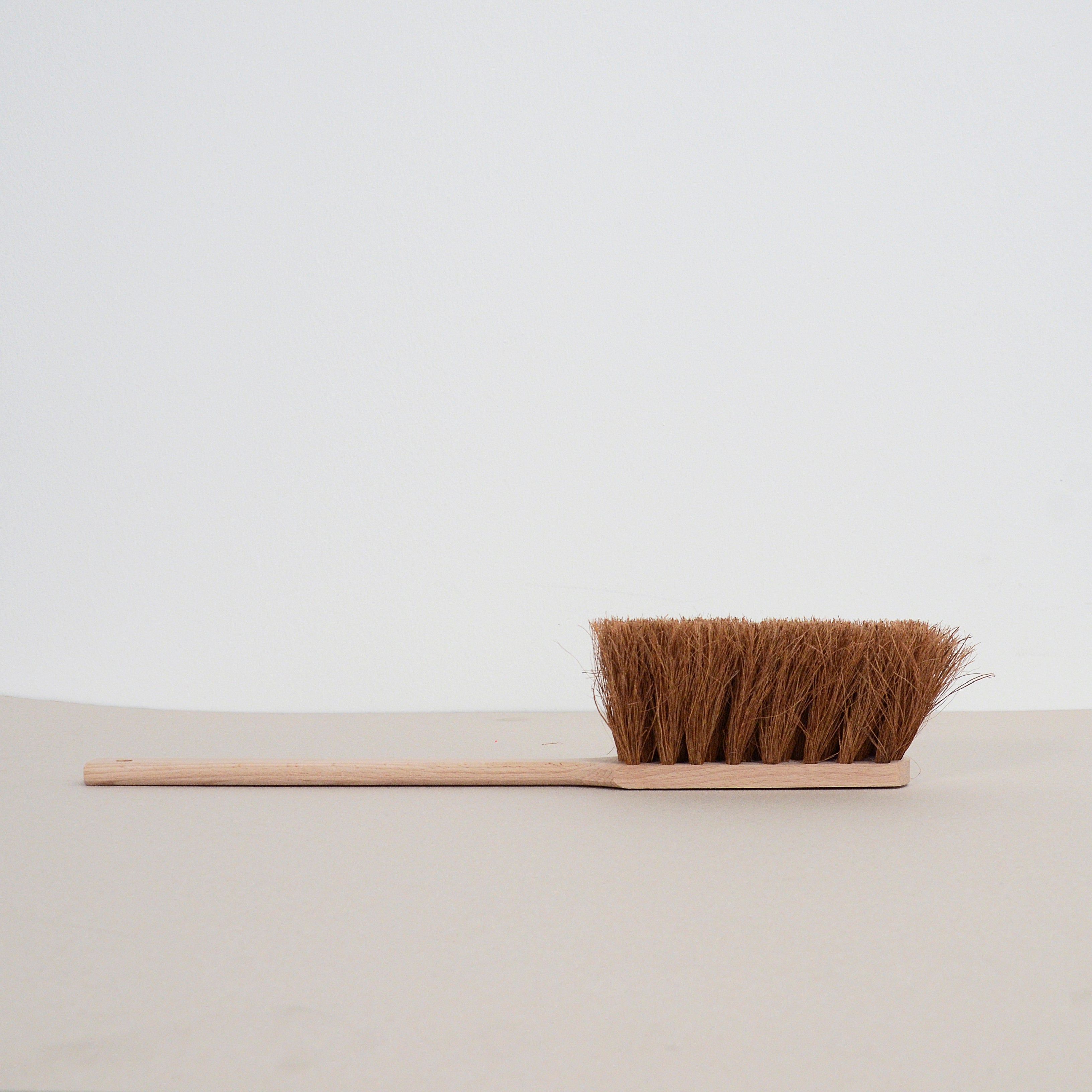 The Hands On brush by GoodGoods features dense brown coconut fiber bristles and a wooden handle crafted from beech wood, showcased horizontally against a minimalist background to highlight its natural materials.