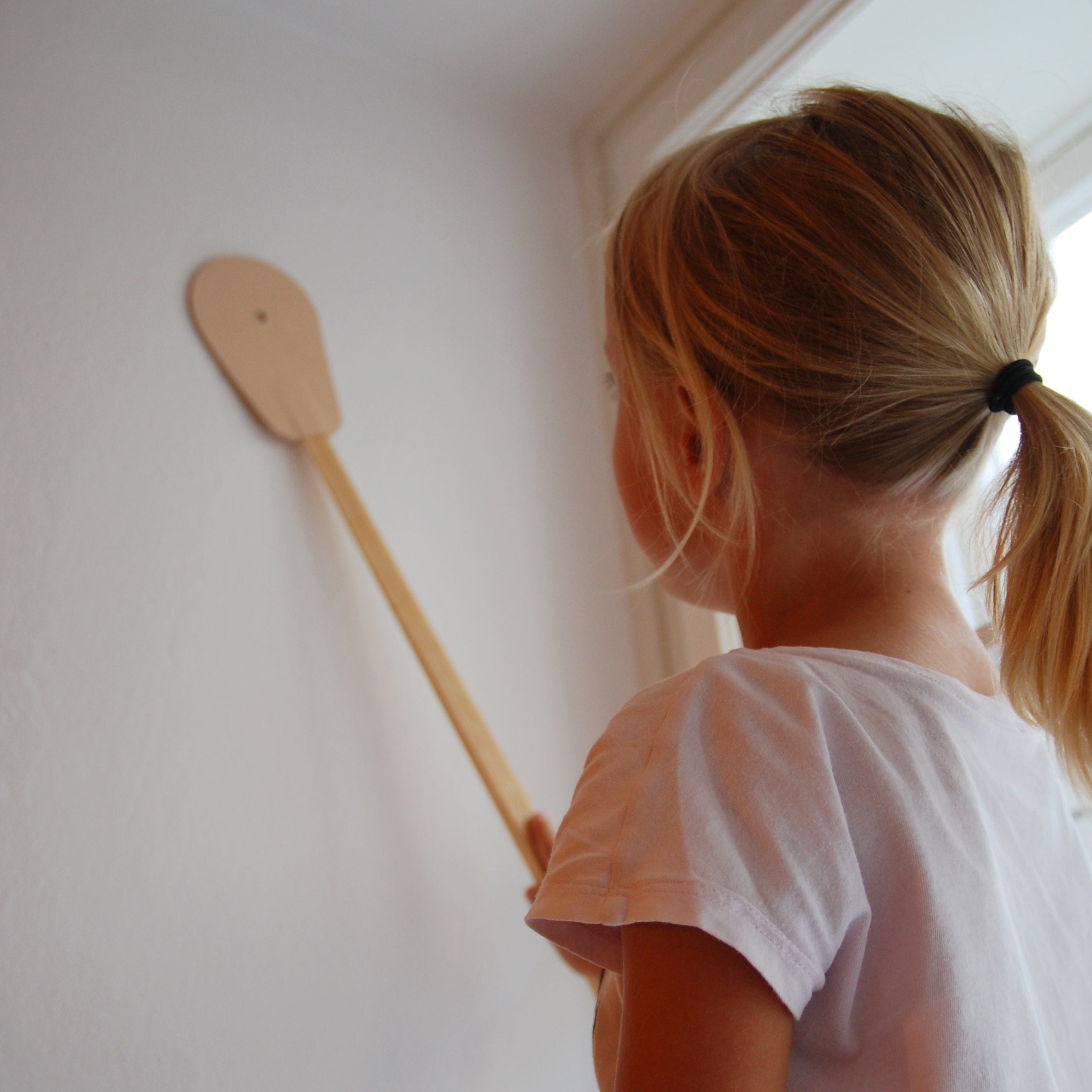 Indoors, a young girl with a ponytail in a light-colored shirt curiously holds the GoodGoods Hit, imagining its aerodynamic potential as she examines it against a white wall.