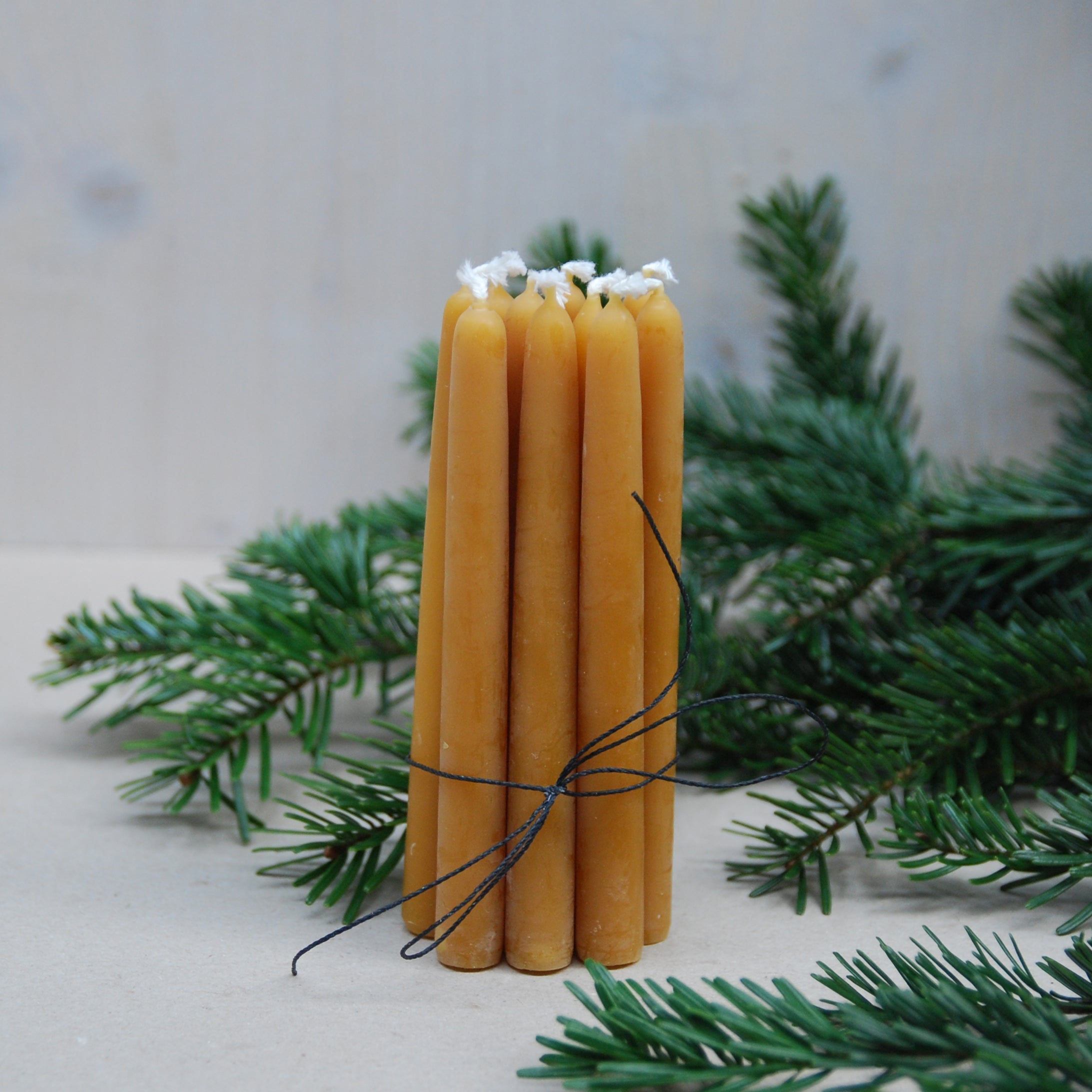 Five handmade beeswax candles from GoodGoods, branded as Light, are bundled with black string and stand upright on a light surface, surrounded by evergreen branches for a festive, natural touch.