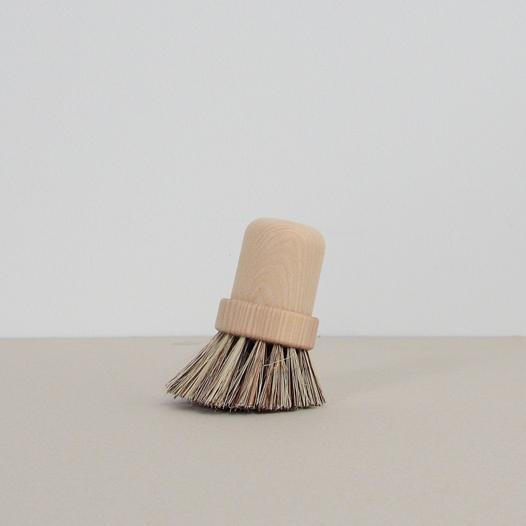 The GoodGoods Pisa pot brush features natural palm fiber bristles and an ash wood handle, standing upright against a plain light background.