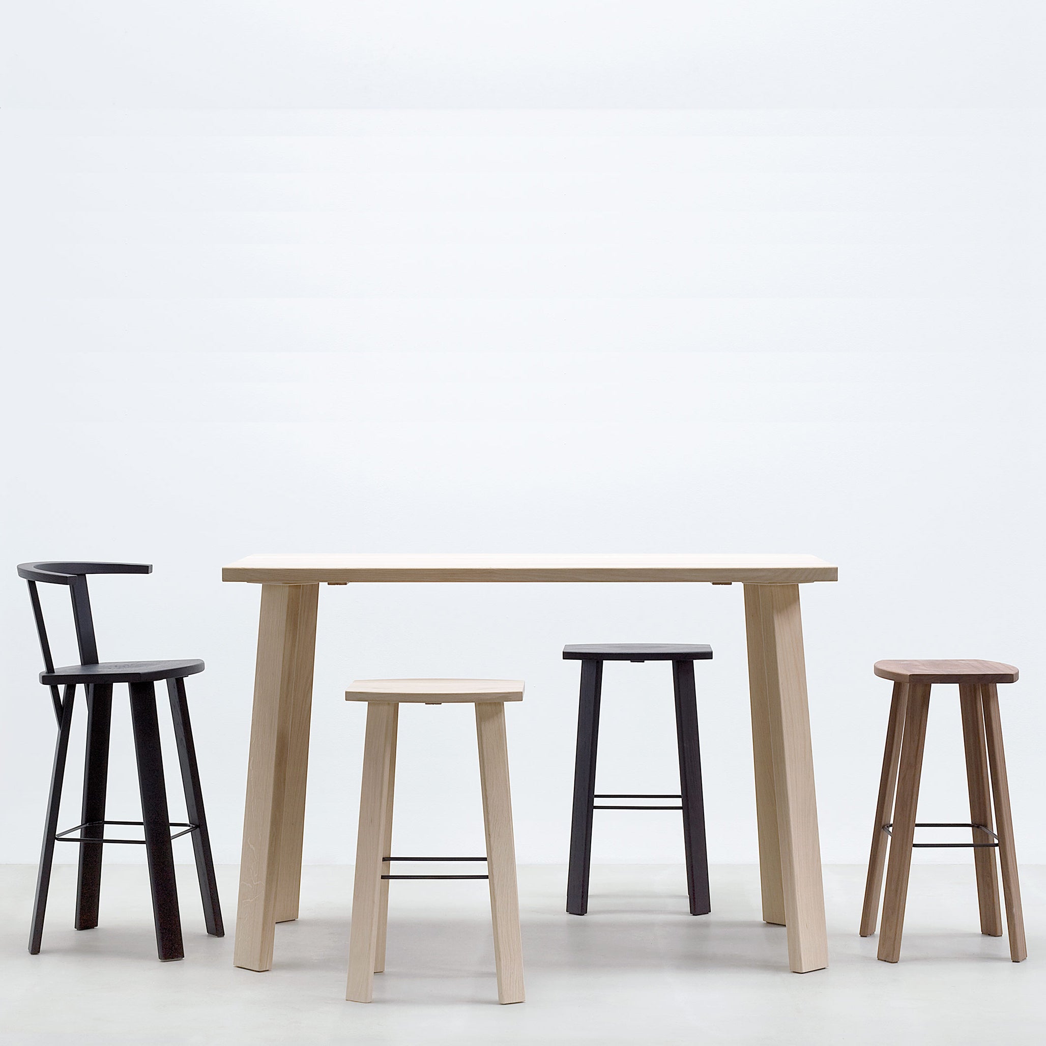 A minimalist setup showcases a light wooden high table with four Alpin Barstools with Armrests by Hussl, featuring varying heights and colors. Set against a plain white background, the furnitures simplicity and sleek design are highlighted.