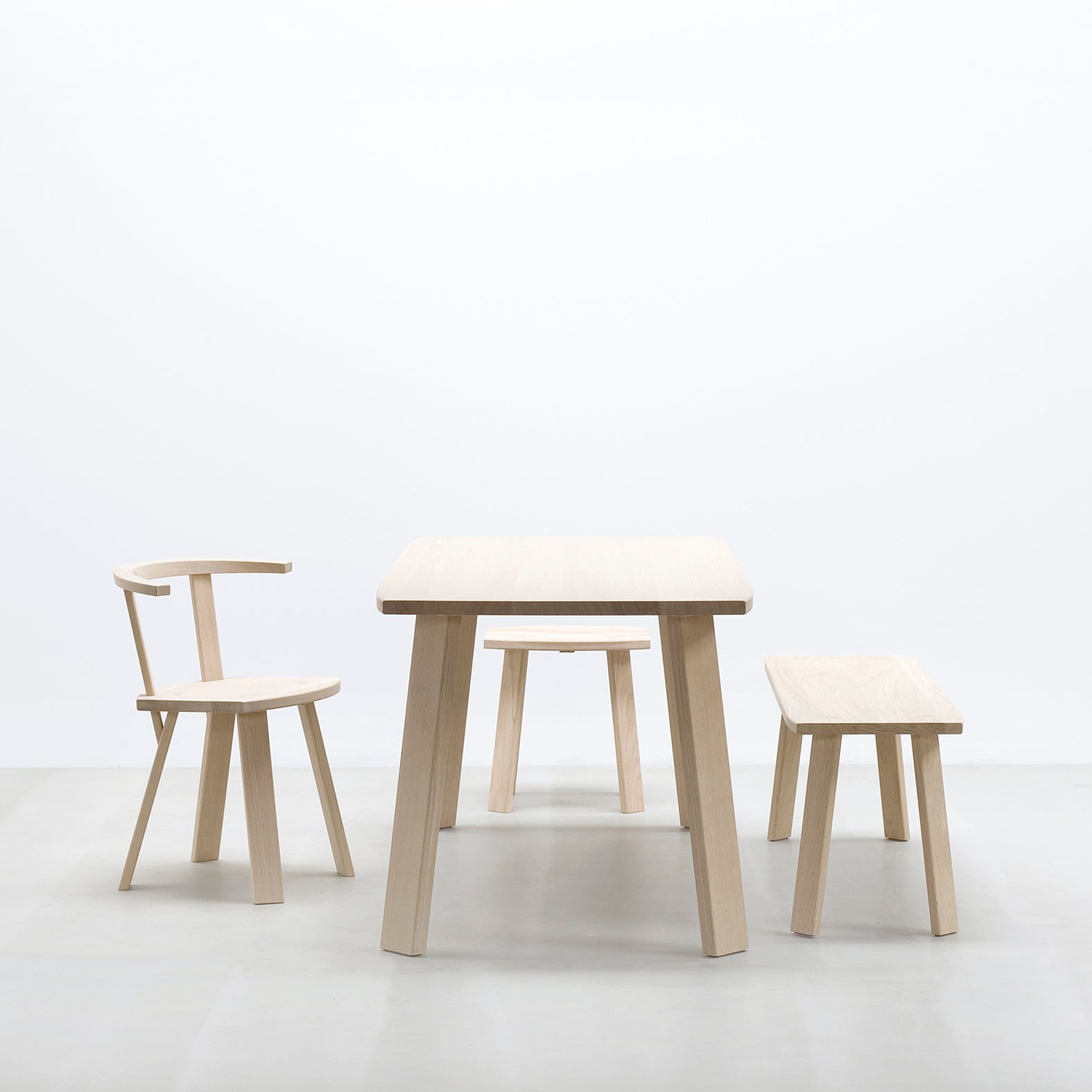 The minimalist furniture set includes the Alpin Bench by Hussl, featuring light wood elements like the Hussl Alpin table. A curved-backrest chair sits elegantly on a light gray floor against a white background. Designed by EOOS, its simple yet modern and inviting.