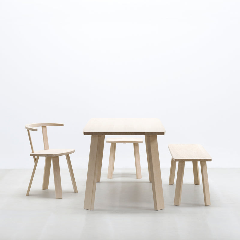 The Hussl Alpin furniture set, featuring the light wood table and the upholstered Alpin Armchair with a curved backrest on the left, pairs elegantly with a simple bench on the right. Set against a plain white background, it highlights its clean, modern design by EOOS.