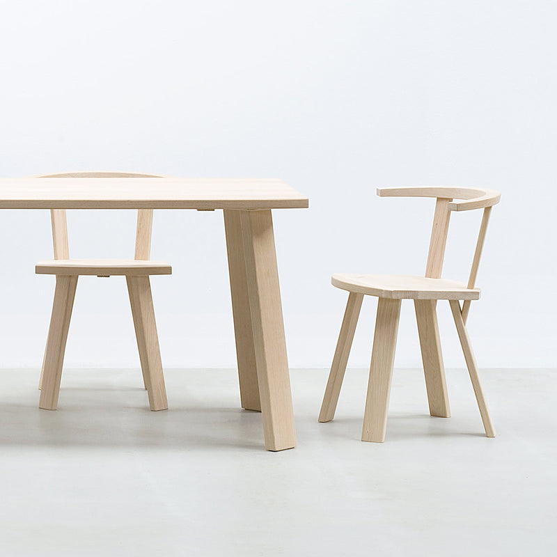 The Hussl Alpin collection includes a minimalist set with a light wood table and two EOOS-designed chairs. The Alpin Armchairs feature upholstered seats, curved backs, and angled legs, perfectly complementing the tables modern design against a plain white background.