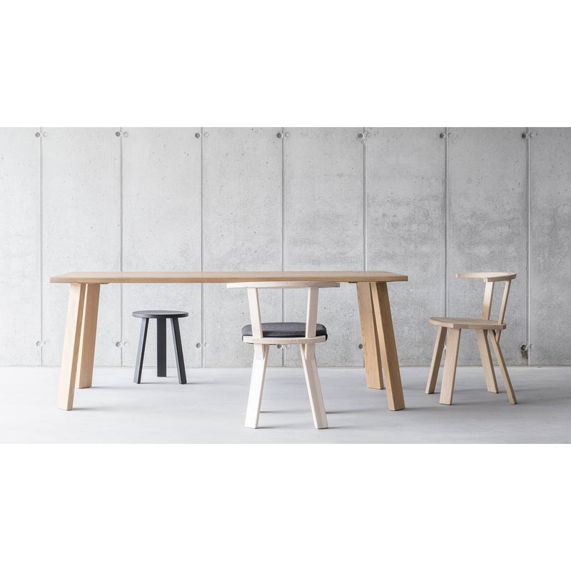 The Alpin Table, by Hussl, paired with two contrasting chairs—one light wood and one dark-cushioned—and a small black stool, creates an elegant EOOS look against a minimalist concrete backdrop, epitomizing the Alpine aesthetic.