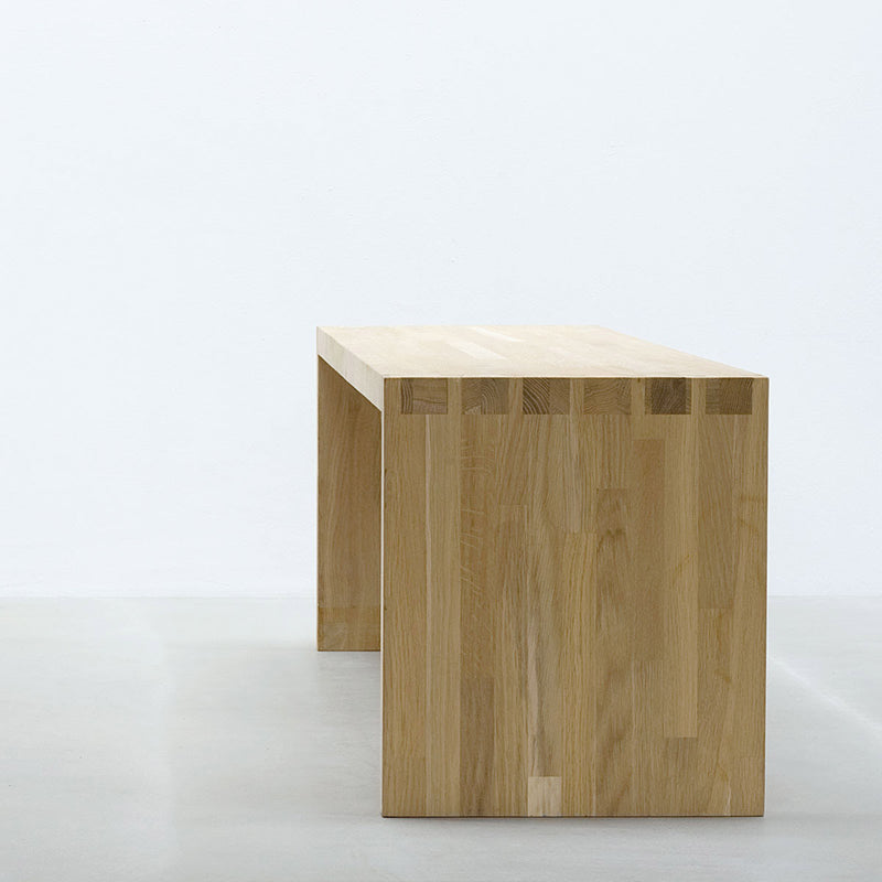 A Hussl bench by Hussl, showcasing a minimalist design with visible dovetail joints, crafted from timber. It rests against a plain white wall on a light gray floor.