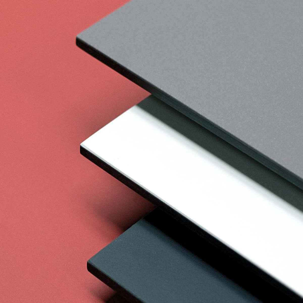 The Lino T by Hussl features three stacked sheets in gray, white, and black against a red background, resembling a sleek linoleum table. Their aligned edges showcase contrasting hues and thickness for a modern tabletop touch.
