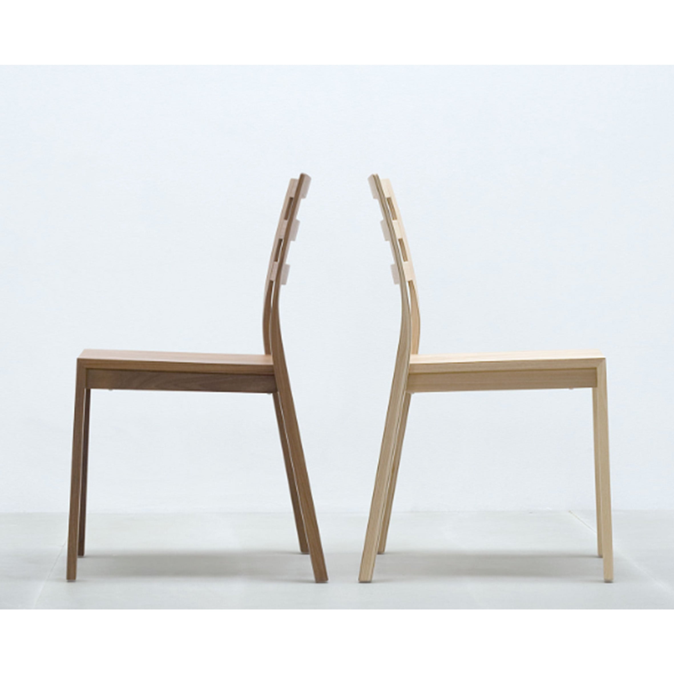 Two Hussl ST10 stackable chairs with a minimalist design are placed back-to-back against a white wall. Featuring straight legs and slightly curved backrests, these chairs offer modern, sleek style and convenience.