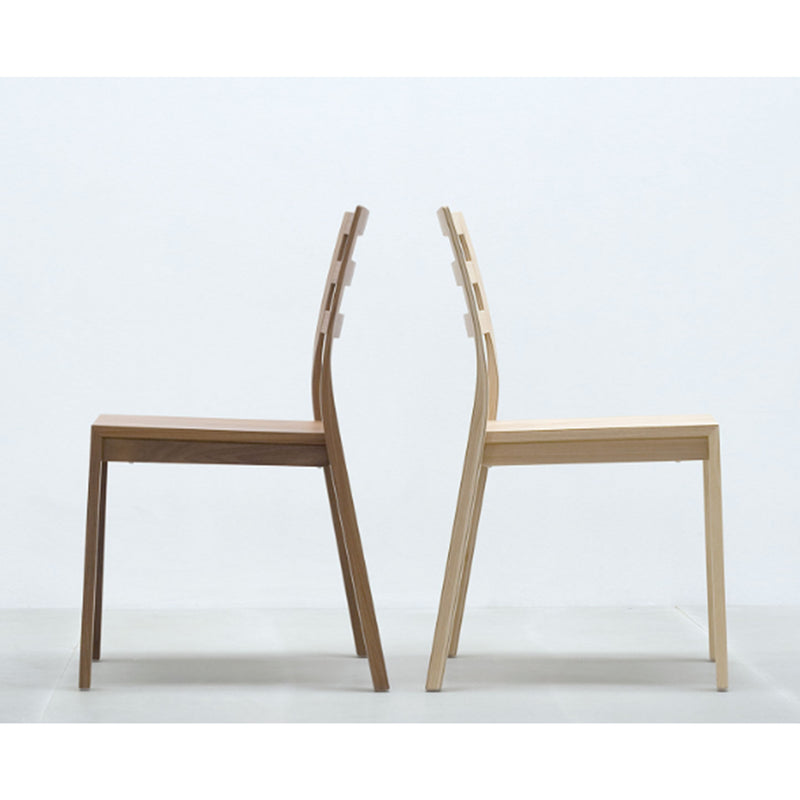 Two Hussl ST10 stackable chairs with a minimalist design are placed back-to-back against a white wall. Featuring straight legs and slightly curved backrests, these chairs offer modern, sleek style and convenience.