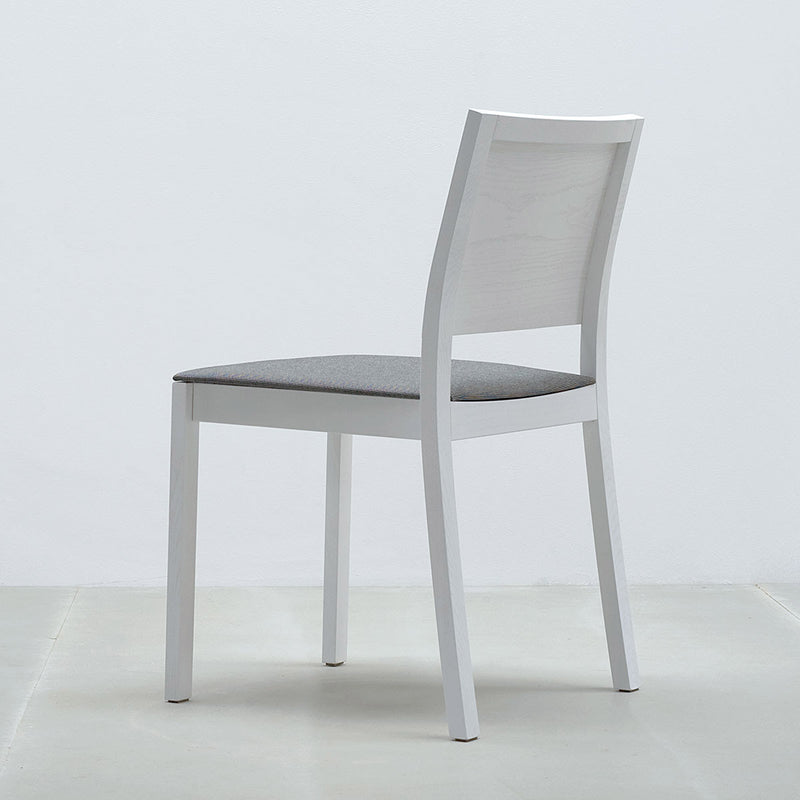 The ST4N Chair Upholstered by Hussl features an ergonomic design with a white solid wood frame and a gray cushioned seat, showcased on a light-colored floor against a plain white background for a simplistic, elegant look.