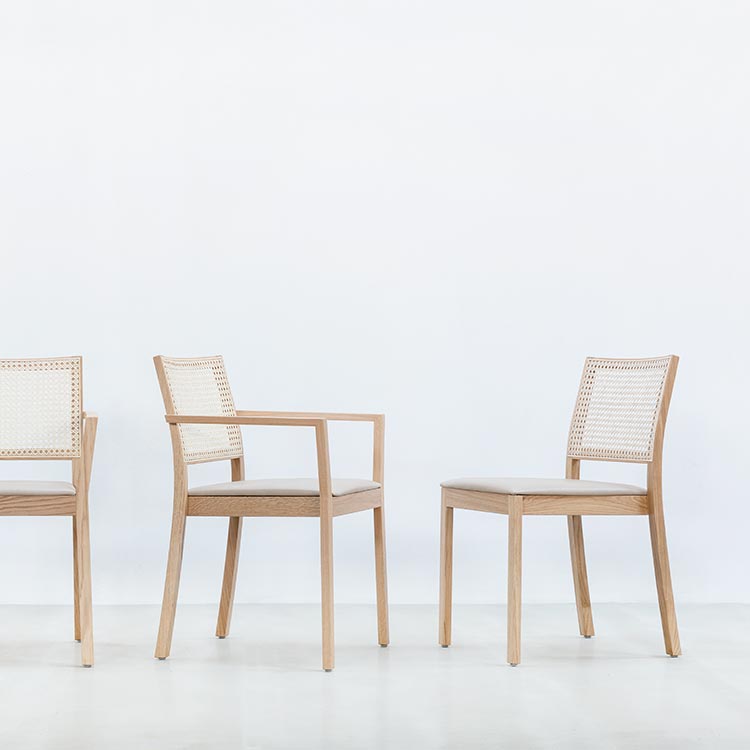 Three ST4N Gritsch wooden chairs by Hussl, featuring Viennese weave backrests, are styled on a light floor with a white background. The coffeehouse furniture showcases simple, modern designs, and the middle chair includes armrests.