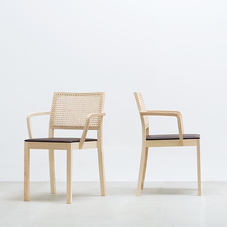 Two Hussl ST4N Gritsch Armchairs with Viennese weave backrests and armrests are displayed in a minimalist setting. One faces forward; the other from the side, both with dark cushioned seats against a light background—perfect for coffeehouses or Café Bistro Gritsch décor.