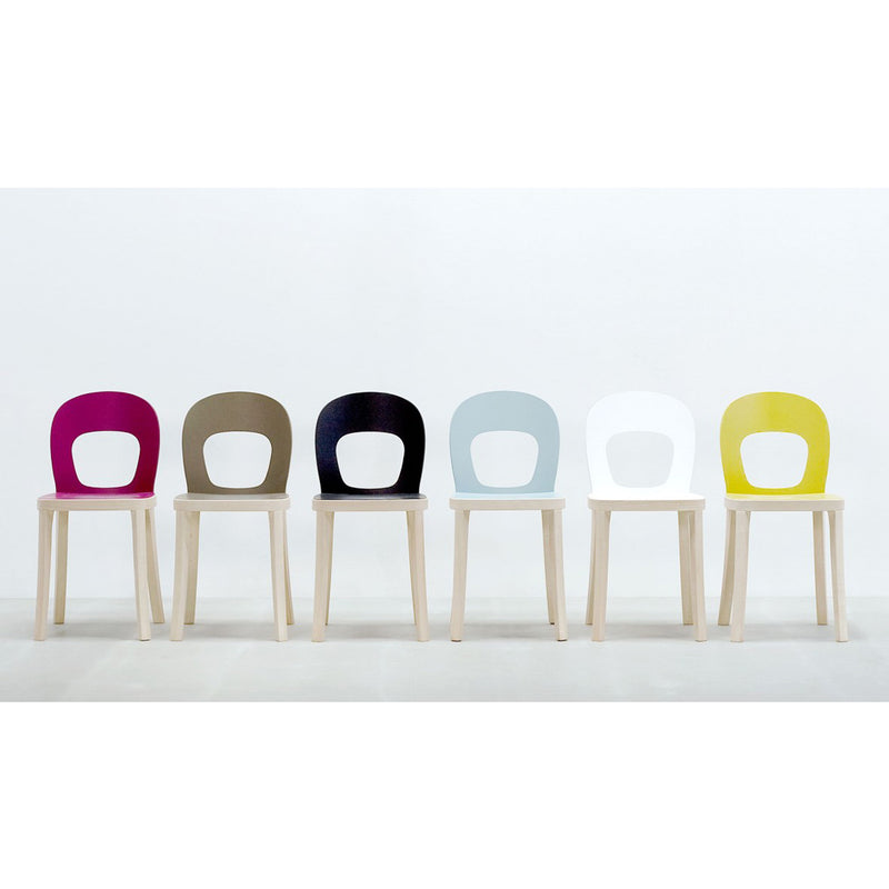 Six Hussl ST6N-1 chairs with wooden legs are lined up against a light backdrop, reminiscent of classic Austrian coffee house settings. They have rounded backrests in magenta, brown, black, light blue, white, and yellow finishes and are both stable and functional.