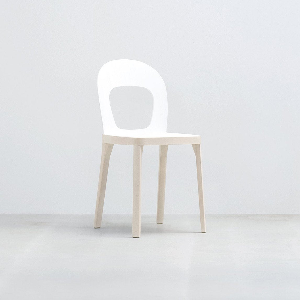 The ST6N-1 by Hussl is a minimalist white chair featuring a circular open backrest, four straight legs, and a flat seat. Reminiscent of Austrian coffee house furnishings, it offers stability and elegance against a plain white background.