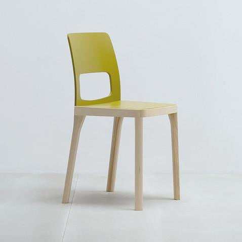 The ST6N-2 by Hussl is a minimalist chair with a light wooden frame, green backrest, and rectangular cutout, capturing the stylish elegance of Austrian coffee house furnishings. Set against a plain, light-colored background, it offers both charm and simplicity.