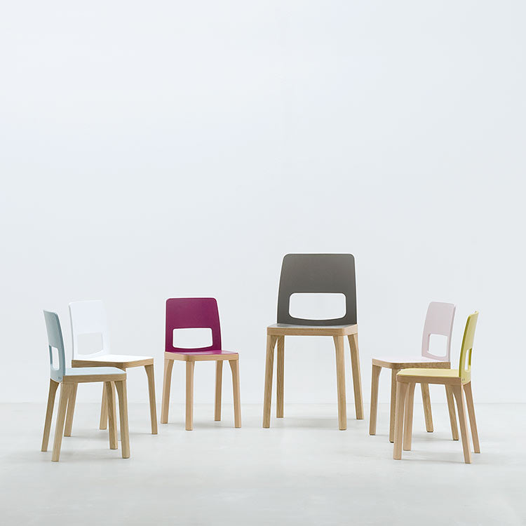 A stylish set of six modern wooden chairs, ST6N-2 by Hussl, features colorful backs—white, blue, purple, grey, pink, and yellow—in a circle on a smooth light floor. These chairs evoke the charm of Austrian coffee house furnishings against a plain background.
