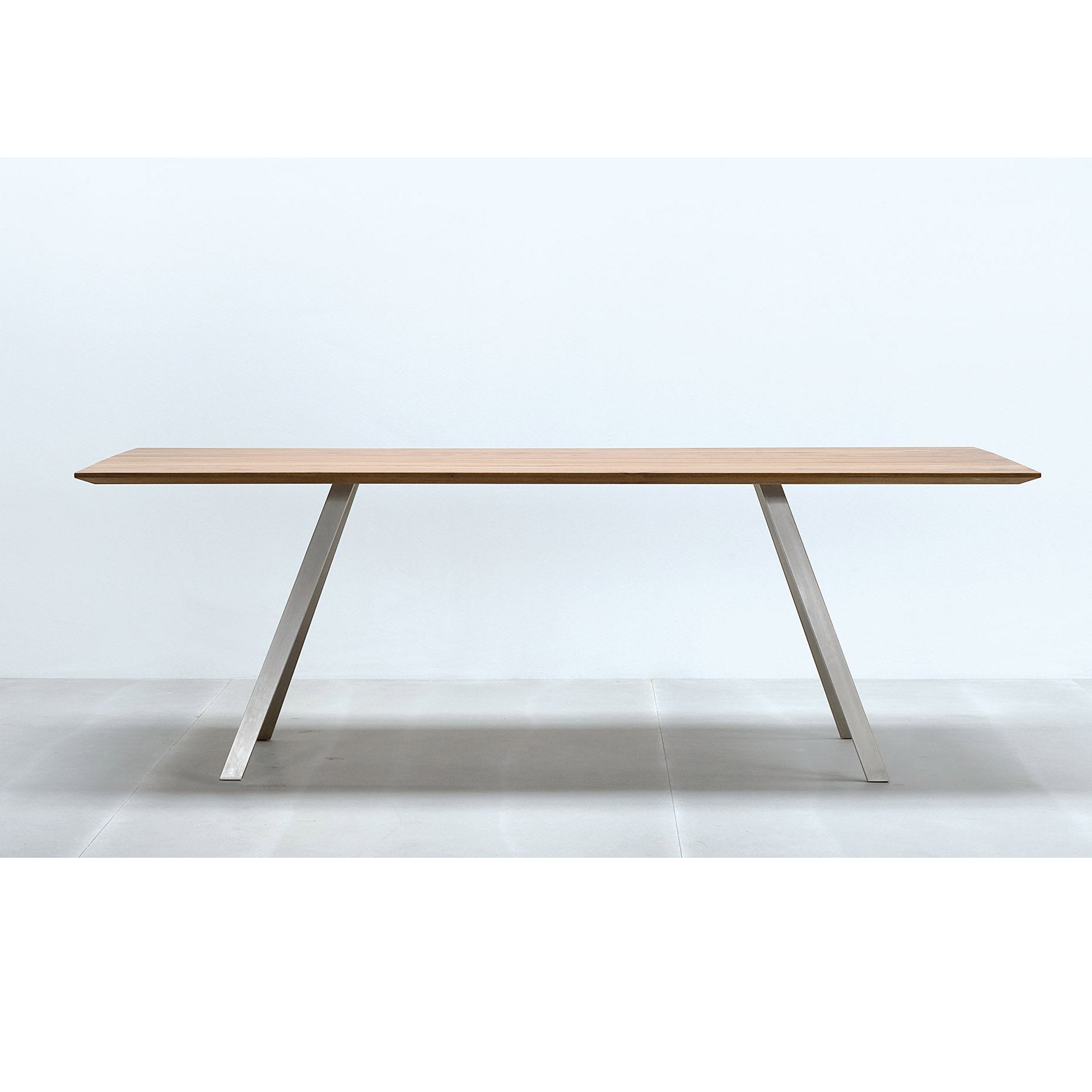 The Solid T Round by Hussl is a minimalist wooden table with a solid wood tabletop and angled, powder-coated steel legs. Its sleek design is set against a plain white background, showcasing the elegance and simplicity of this modern furniture piece.